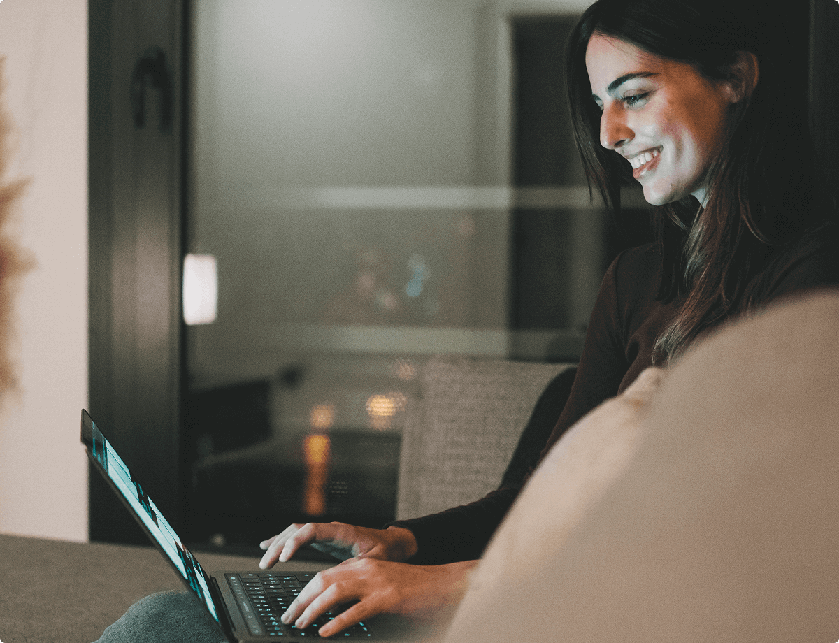 A brunette woman is sitting on a couch using her laptop. She has used her VPN to change her IP address, making her safer as she browses.