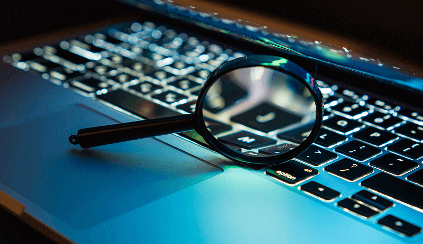A magnifying glass on a laptop keyboard illustrates Usenet search tools made available by UsenetServer.
