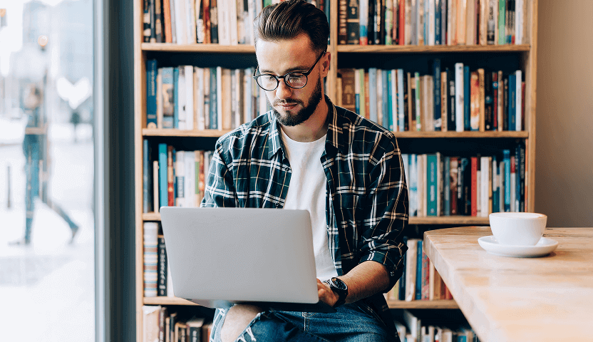 A man on a laptop sits in a coffee shop, browsing Usenet newsgroups with UsenetServer’s premium Usenet access.